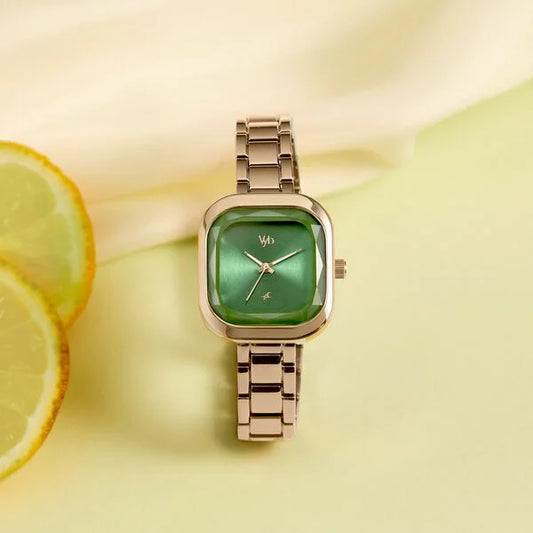 Gold watch with a green face on a yellow background with lemon slices